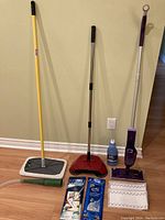 Full view of all cleaning equipment and supplies lined up against wall, showing mops, sweepers, cleaning wipes and vacuum attachment.