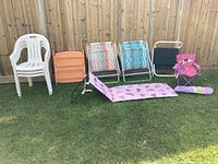 Variety of outdoor chairs and lounger seats in a grassy backyard setting against a wooden fence