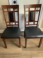 Pair of wooden dining chairs featuring vertical and horizontal wooden slats with black upholstered padded seats and backs.