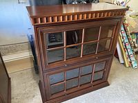 Front view of wooden display cabinet showing two glass doors with wood pane framing and decorative top edge.
