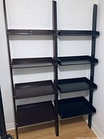 Front view of two leaning display shelves side by side, one lighter brown with scratches and one darker brown/black
