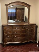 Front view of dresser with attached large arched mirror showing wood finish, drawer handles, and minor wear.