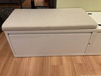 Front view of the white metal filing cabinet with beige fabric padded seat cushion attached on top, showing clean lines and a large drawer front.