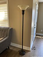 Full view of the floor lamp showing its height and placement next to a couch, with the cream-colored frosted glass torchiere shade and slim metal pole visible.