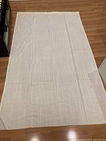 Full view of one off-white curtain panel laid flat on floor showing size and subtle woven texture.