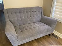 Front view of gray fabric love seat with tufted cushions, angled arms and wooden legs.