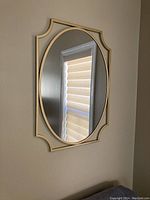 Front view of the oval mirror on the wall showing decorative gold-tone frame and reflective surface.