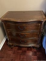Front view of wooden nightstand showing three curved drawers with metal handles and overall dark brown finish.