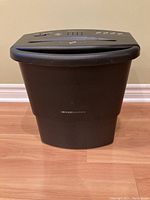 Front view showing black Concept Solutions waste basket with paper shredder top sitting on it.