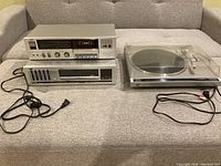 Wide shot of the three stereo equipment units showing the cassette deck, receiver, and record player with cords.