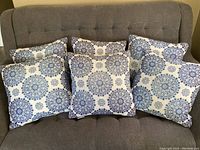 Six square throw pillows on grey couch showing detailed blue mandala pattern on white background.