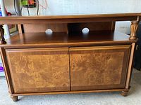 Front view of wooden TV cabinet showing two cabinet doors with wood grain pattern and open shelf with wire management holes.
