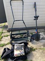 Yardworks push reel mower, Toro electric trimmer, and two Toro mower covers laying on stone slab with shed background