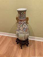 Full view of porcelain vase on wooden stand, showing painted scenes and gold handles