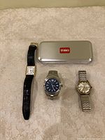 Photo of four wrist watches and closed Toro metal case on cream patterned fabric
