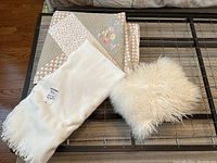 Photo of the folded floral quilt, white fleece throw with tag, and cream faux fur cushion on a metal frame surface.