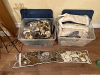 Two clear plastic bins with dark blue lids containing various Christmas decorations including stockings, faux floral arrangements, and garland.