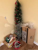 Artificial Christmas tree with decorations next to packaging boxes and accessories on floor