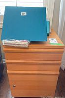 Front view of wooden desk pedestal file cabinet with blue binders and notepad on top. Shows drawer fronts and lock.