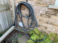 Coiled garden hose with attached spray nozzle hanging on an outdoor wall next to a door and small plants under it.