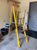 Front angled view of the yellow Fiber-Lite ladder with four metal steps, standing open in a garage.