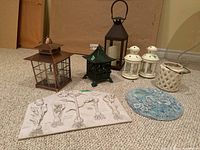 Full view of all lanterns including Asian cast iron, metal, ceramic lanterns, and two resin garden plaques visible on carpeted floor.