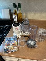 Full lot on kitchen counter showing Magic Bullet Plus blender motor base, blending cups, recipe book, decorative bottles and stand