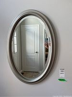 Front view of oval beveled edge mirror mounted on wall showing reflection of door and hallway.