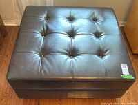 Top view showing dark brown leather-like upholstery with button tufting in a 3x3 grid pattern, square shape with smooth edges.