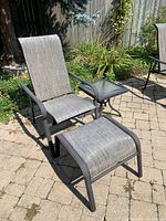 Metal and plastic mesh reclining patio chair with ottoman and glass top side table on stone patio