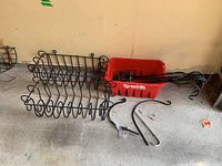Photo showing two black wrought iron rectangular plant holders with scrollwork design, several black metal shepherd's hooks, and a red plastic tub holding some hooks.