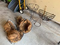 Four metal wireframe hanging plant holders with natural fiber coco liners placed on the floor with one tall metal plant stand.