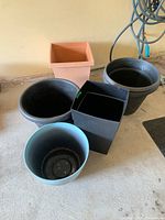 Five plastic planters of various shapes and sizes grouped together on a concrete floor.