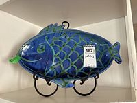 Front view of blue and green glazed fish-shaped ceramic platter on metal stand.