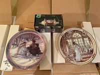 Collector plates shown in open cardboard packaging with box for porcelain ornament visible in background.