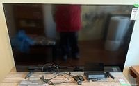 Front view of 55" TV on table with cables, remote and Blu-ray player in front