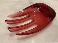 Photo of red translucent acrylic tray shaped like an abstract hand showing fingers and thumb compartments with mild scratches.