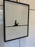 Photo of framed Joanna Ham 'DJ Rabbit' print hanging on a wall, showing black silhouette rabbit DJ on white background with thick horizontal black line.