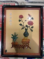 Full view of the framed hand-carved stone picture showing floral and artifact elements on wooden stands.