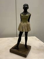 Front view of the vintage statue of young ballet dancer on a marble surface, showing dancer with hands behind back and full tutu.