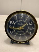 Front view of vintage WESTCLOX Baby Ben clock showing black clock face with white jeweled numerals and gold hands, with noticeable surface wear and scratches on clock face and casing.