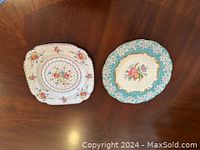 Two Royal Albert dinner plates on a wooden table, one square Petit Point and one round Enchantment pattern.