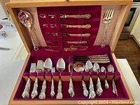 Complete 18-piece silverware set in maple wood box with purple velvet lining, showing knives, forks, spoons, and serving utensils.