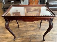 Photo showing full front and side view of small sofa table with carved cabriole legs and glass top, highlighting the detailed carvings and wood finish.