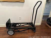 Black metal convertible hand cart/dolly in excellent condition, showing the side view with handle upright and wheels visible on wood floor.