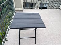 Black metal bistro table showing slatted square top surface and foldable design