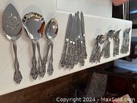 Photo showing various cutlery pieces including cake server, salad servers, serving spoons, knives, and spoons and forks with detailed ornate handles.