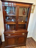 Front view of mahogany china cabinet with glass doors and display shelves inside. Lower cabinet and drawer visible.