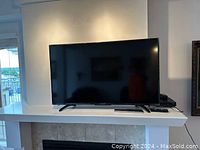 Front of TV on white shelf above fireplace, showing entire unit and remote