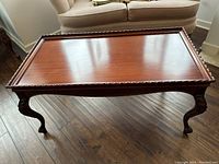 Full view of the polished wooden coffee table top showcasing the carved edge detail and cabriole legs.